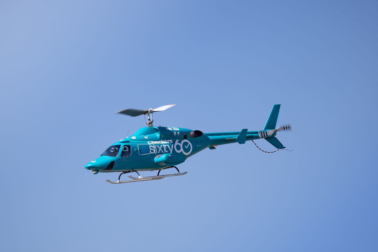 A striking blue helicopter hovering against a backdrop of clear blue skies.